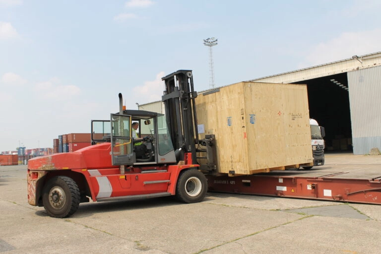 Eine Industrieverpackung aus Holz wird mit einem roten Gabelstapler für den Transport auf eine Rampe gehoben.